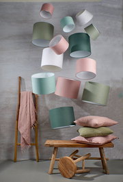 Mehrere runde Lampenschirme in verschiedenen Farben schweben in der Luft. Im Vordergrund sind eine Holzbank, ein Hocker und Kissen zu sehen. Die Perspektive ist leicht von unten.