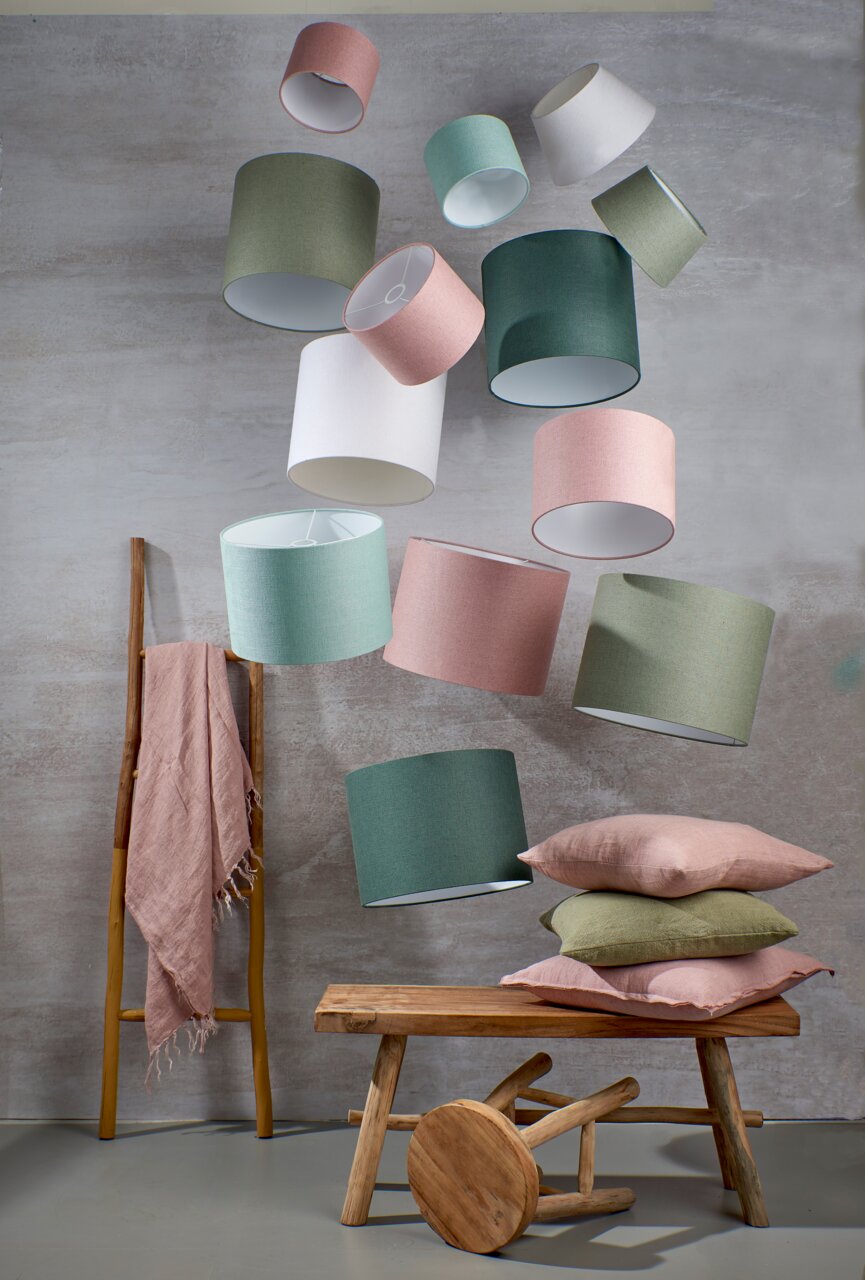 Mehrere runde Lampenschirme in verschiedenen Farben schweben in der Luft. Im Vordergrund sind eine Holzbank, ein Hocker und Kissen zu sehen. Die Perspektive ist leicht von unten.