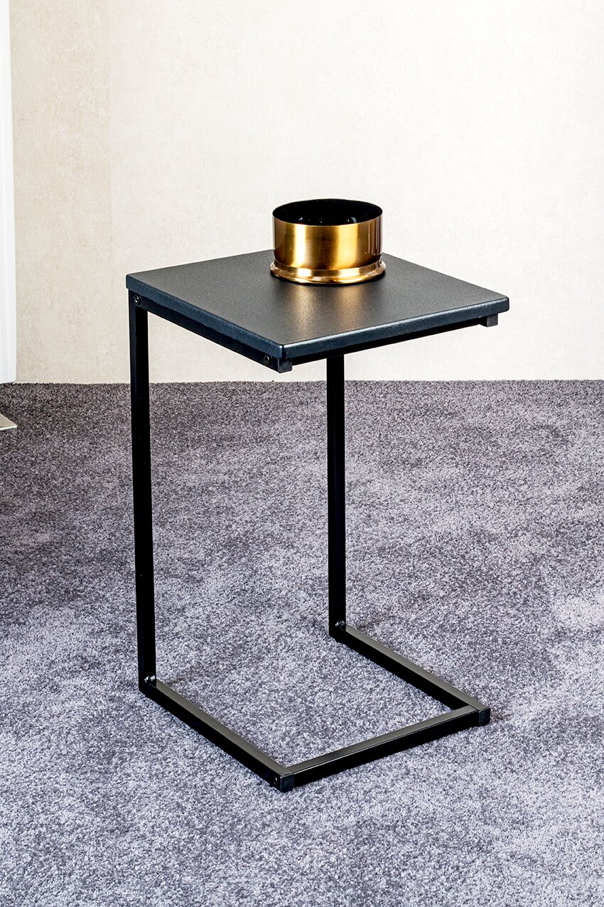 Schwarzer, minimalistischer Beistelltisch aus Metall mit U-förmigem Gestell auf grauem Teppich, darauf eine goldene Schale; fotografiert aus leicht erhöhter Front-/Schrägansicht.