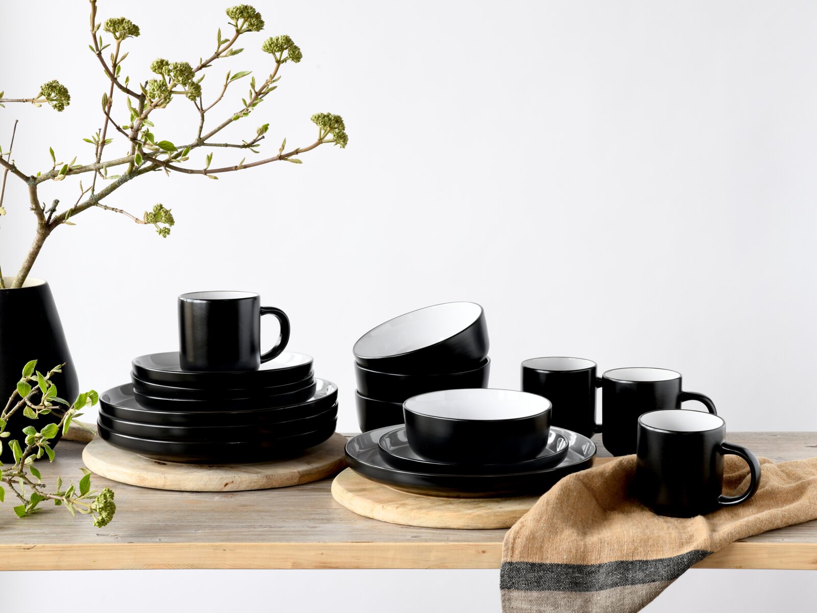 Creatable Kombiservice 16-tlg NORDIC Schwarzes, mattes Geschirrset mit Tellern, Schalen und Tassen auf Holzbrettern, fotografiert in frontaler Perspektive mit leichter Draufsicht vor hellem Hintergrund.