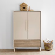 Moderner Kleiderschrank mit zwei Türen und einer Schublade, frontal fotografiert. Obenauf steht ein dekoratives Korbhaus und ein kleines Spielzeugauto. Daneben befindet sich ein geflochtener Korb mit Kissen.
