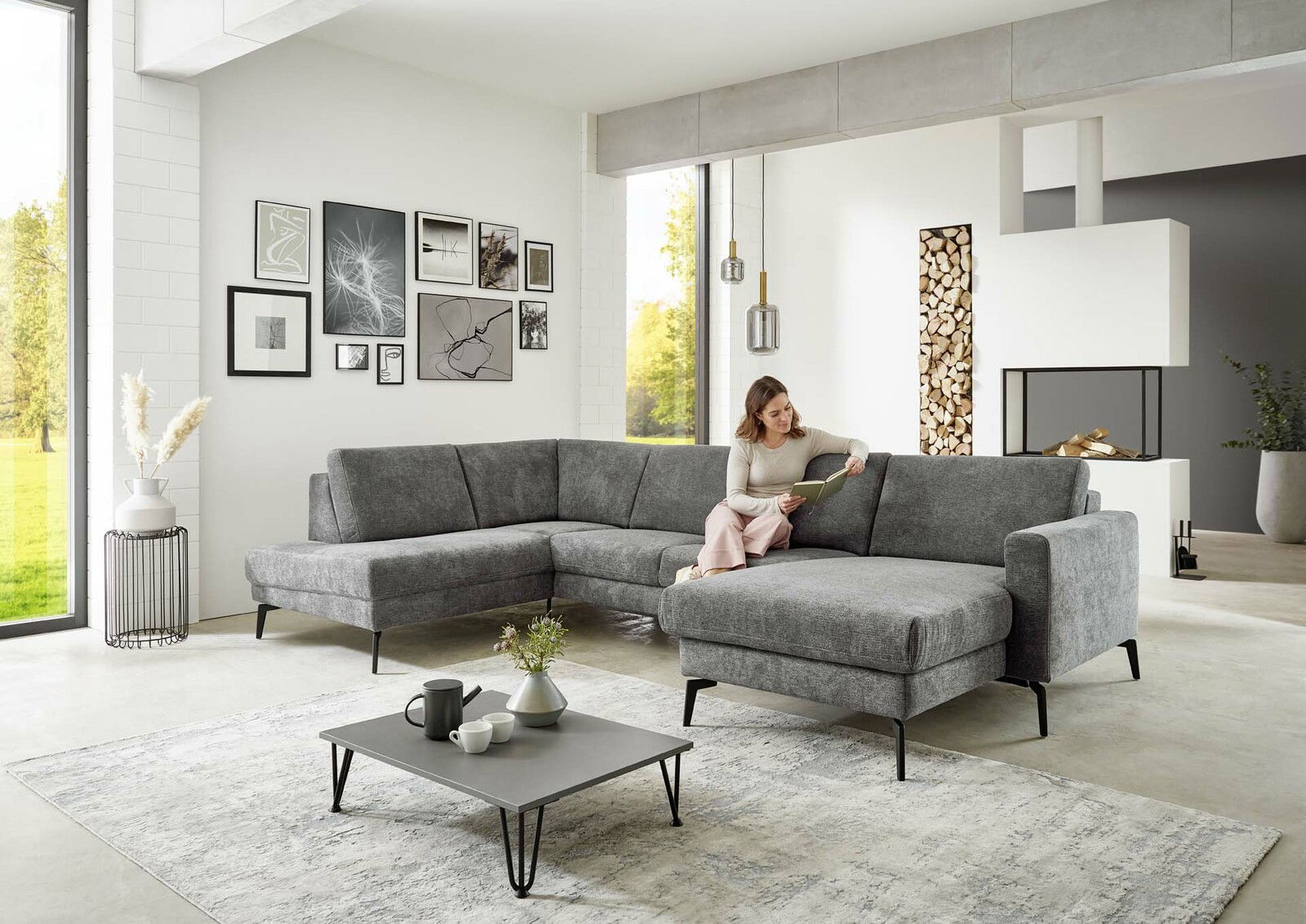 Graue Polsterrundecke in modernem Wohnzimmer, seitliche Perspektive, mit einer Frau, die auf dem Sofa sitzt und ein Buch liest.