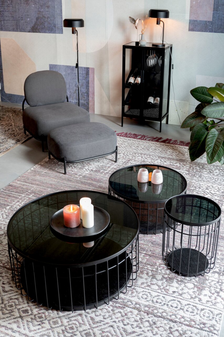 Moderner Wohnbereich mit einem Set aus drei runden Tischen mit schwarzem Metallgestell und Glasplatte, dekoriert mit Kerzen und Vasen, aus der Vogelperspektive betrachtet.
