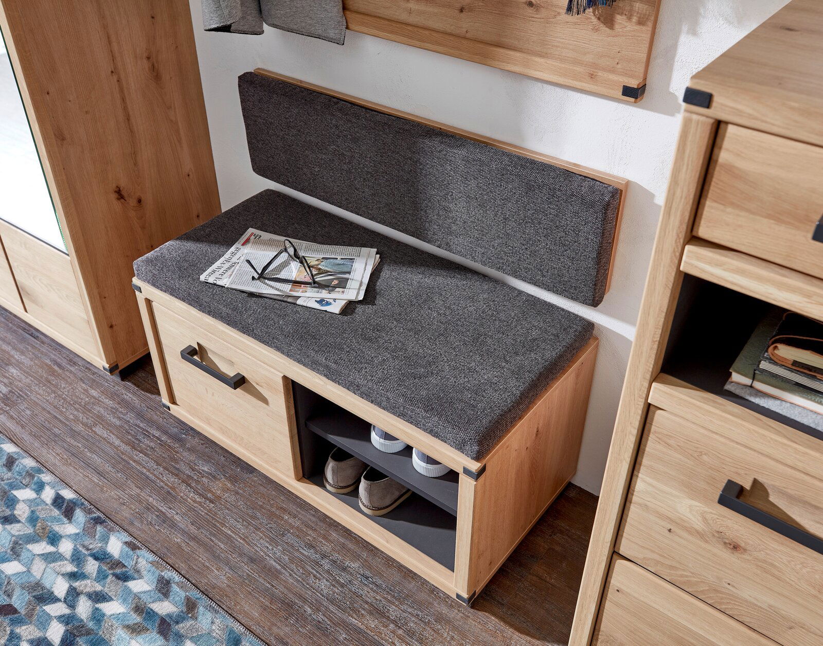 Garderobenbank aus Holz mit grauem Polster, zwei Schubladen und offenen Fächern, seitliche Perspektive