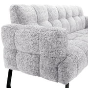 Detailaanzicht vanuit schuin vooraanzicht van een lichtgrijze, gemêleerde fauteuil met zachte blokstiksels, brede armleuning en zwarte metalen poten