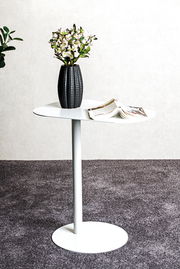 Moderner weißer Beistelltisch mit runder Platte, darauf eine schwarze Vase mit Blumen und ein geöffnetes Magazin, seitliche Perspektive.