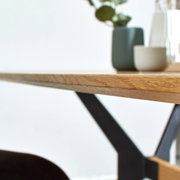 Nahaufnahme eines Esstisches mit Holzplatte und schwarzem Metallgestell, seitliche Perspektive