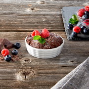 Aufsicht auf eine weiße, geriffelte Auflaufform mit einem Schokoladenkuchen, garniert mit Himbeeren und Minzblättern, auf einem rustikalen Holztisch.