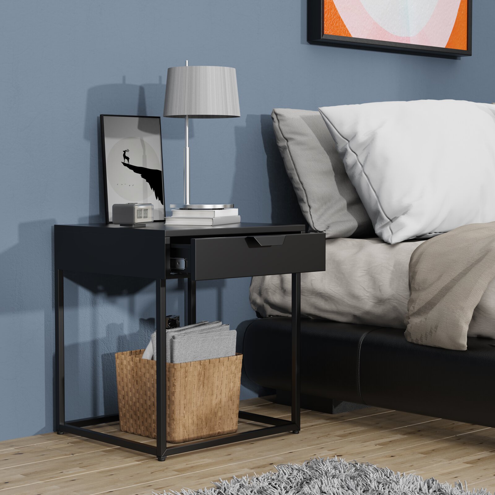 VCM Nachttisch FLOKAS Moderner schwarzer Nachttisch mit Schublade und Metallgestell neben einem Bett, dekoriert mit Lampe, Büchern und Bild; Ansicht schräg von vorn auf Augenhöhe.