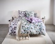 Bettwäsche-Set mit geometrischem Muster in Grau, Blau und Lila auf einem Bett, fotografiert aus der Frontalperspektive.