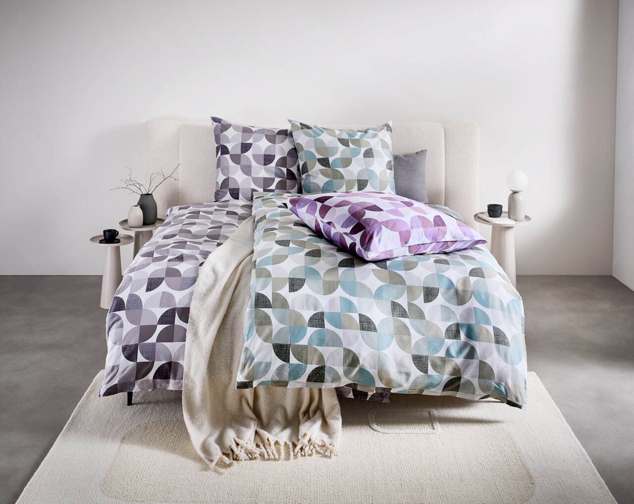 Bettwäsche-Set mit geometrischem Muster in Grau, Blau und Lila auf einem Bett, fotografiert aus der Frontalperspektive.