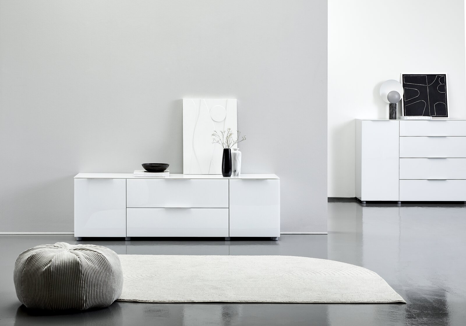 Modernes weißes TV-Lowboard mit Hochglanzoberfläche, frontal fotografiert, dekoriert mit einer Vase und einem Kunstwerk.