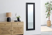 Schwarzer Wandspiegel mit geriffeltem Rahmen, ca. 50x150 cm, in einem modernen Raum mit Kommode, Lampe und Pflanze, seitliche Perspektive.