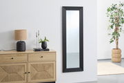 Schwarzer Wandspiegel mit geriffeltem Rahmen, ca. 50x150 cm, in einem modernen Raum mit Kommode, Lampe und Pflanze, seitliche Perspektive.