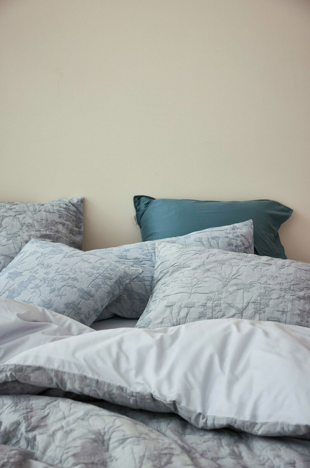 Essenza Home Bettwäsche MARIBEL Bettwäsche-Set mit floralem Muster in Grautönen, bestehend aus mehreren Kissen und einer Decke, aus der Perspektive von der Seite fotografiert.