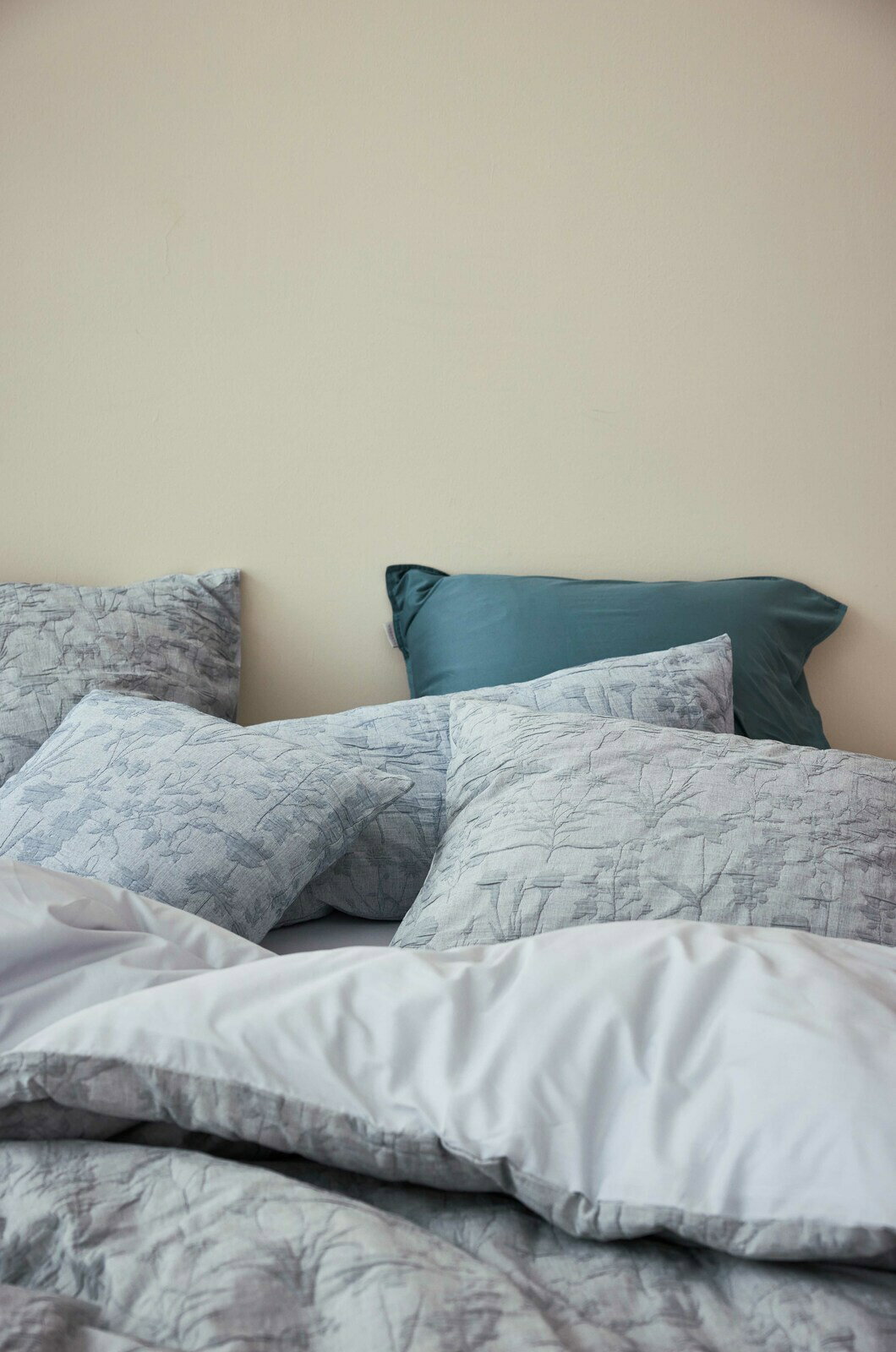 Bettwäsche-Set mit floralem Muster in Grautönen, bestehend aus mehreren Kissen und einer Decke, aus der Perspektive von der Seite fotografiert.