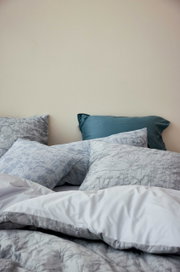 Bettwäsche-Set mit floralem Muster in Grautönen, bestehend aus mehreren Kissen und einer Decke, aus der Perspektive von der Seite fotografiert.