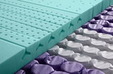 Nahaufnahme einer Wendematratze mit Taschenfederkern, die eine Schicht aus grünem Schaumstoff mit Belüftungslöchern und darunter liegenden lila und weißen Taschenfedern zeigt.
