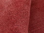 Nahaufnahme eines weichen, runden Teppichs in Rot, perspektivisch von oben fotografiert.