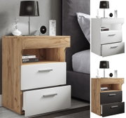 Moderner Nachttisch in Eiche-Optik mit zwei weißen Schubladen, offenem Fach und Metallgriffen, neben einem Bett mit Lampe und Deko, gezeigt in schräger Frontansicht.