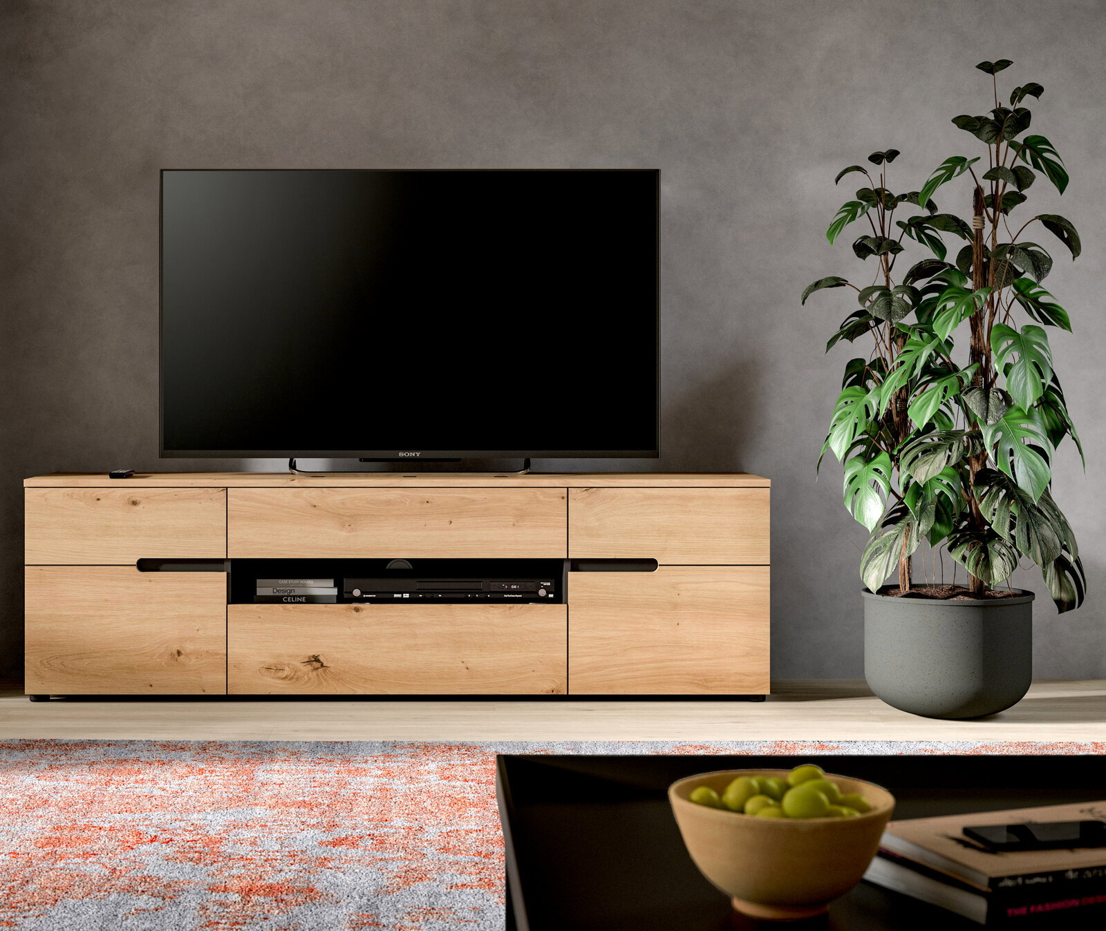MID.YOU TV Lowboard CANU Modernes Wohnzimmer-Setup mit großem Flachbildfernseher auf hellem Holz-TV-Lowboard mit Schubladen und offenem Fach, daneben große Zimmerpflanze im grauen Topf; Frontalansicht auf Augenhöhe.