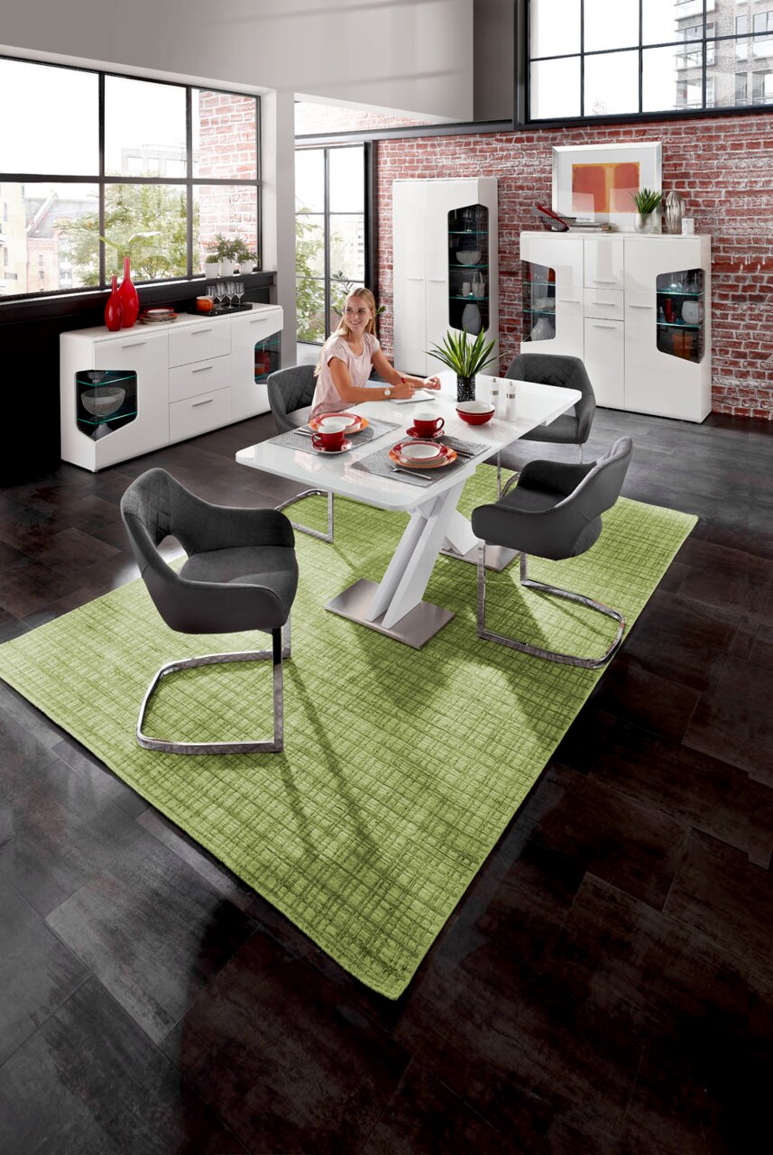 Hom´in Funktions-Esstisch MARTIN Moderne Esszimmer-Szene mit einem weißen Funktions-Esstisch, umgeben von grauen Armlehnstühlen auf einem grünen Teppich. Im Hintergrund sind ein Sideboard und eine Highboard-Vitrine vor einer Backsteinwand zu sehen. Perspektive: Blick von oben auf den Tis