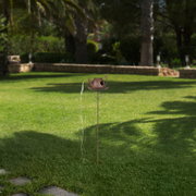 Solarbetriebene Gartenleuchte in Form einer Gießkanne auf einem Stab, seitliche Perspektive im Garten