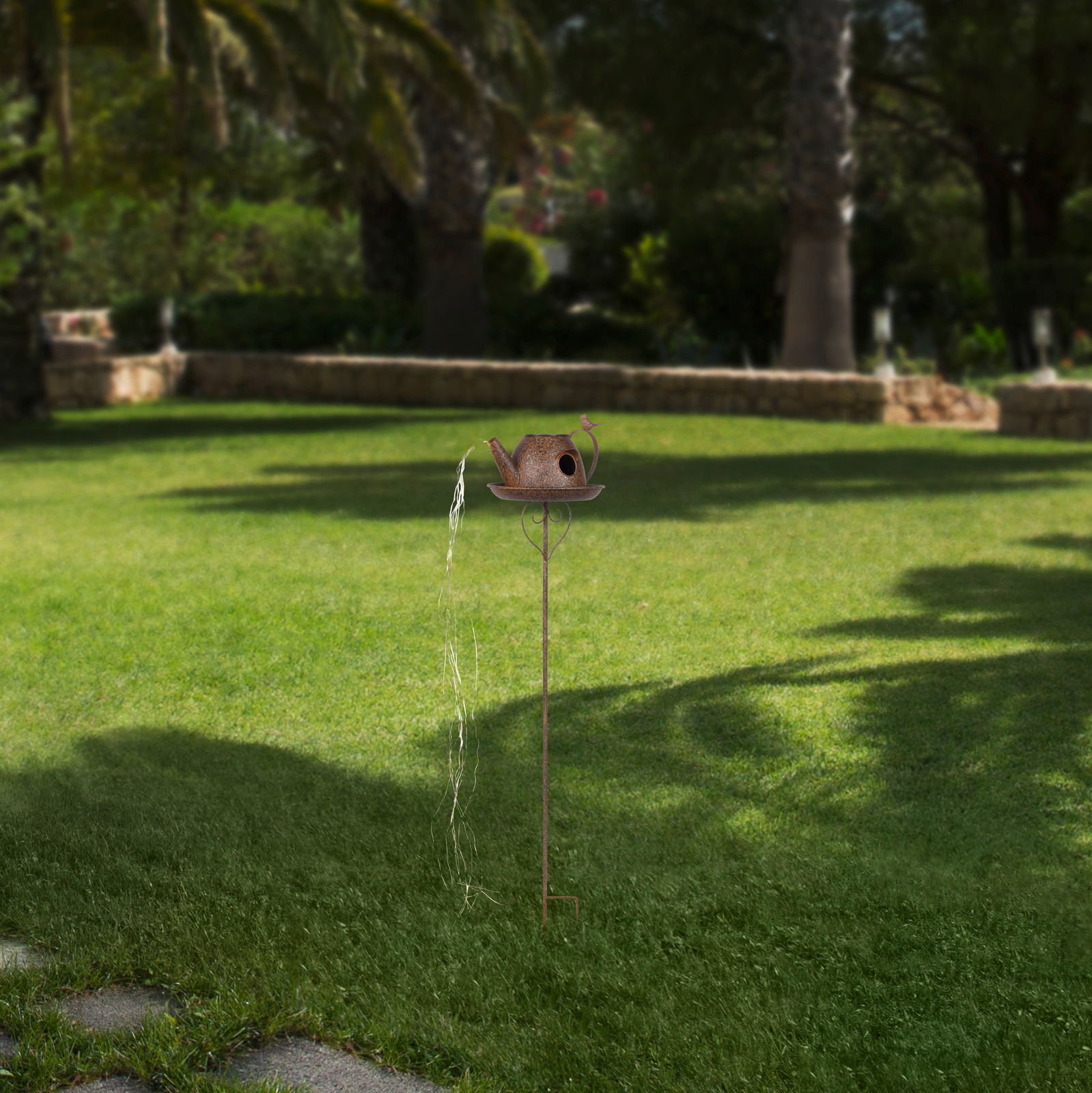 Solarbetriebene Gartenleuchte in Form einer Gießkanne auf einem Stab, seitliche Perspektive im Garten