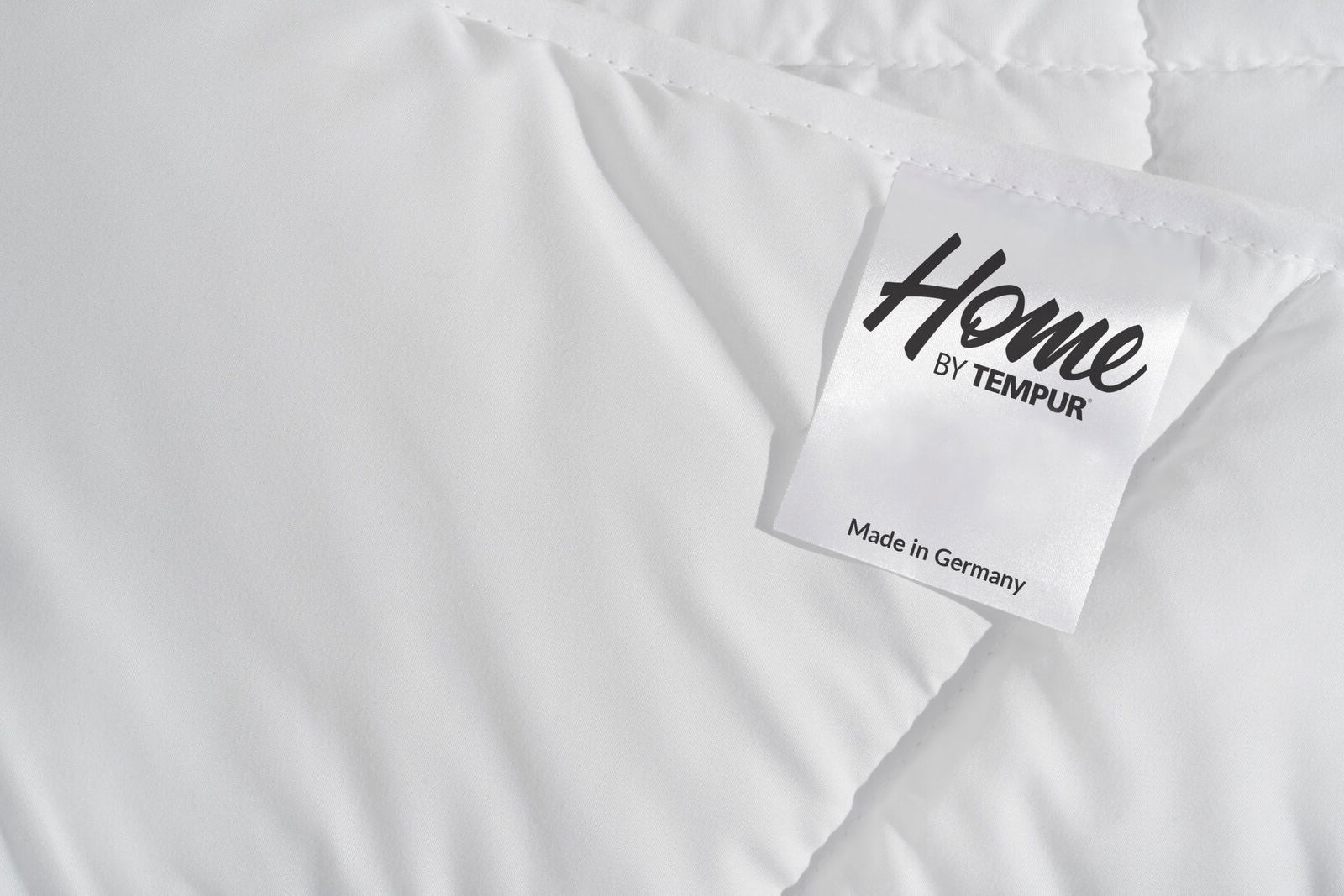 Nahaufnahme einer weißen Luxe Duo-Decke mit einem Etikett, das 'Made in Germany' zeigt.