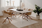 Moderner Esstisch mit heller Tischplatte und weißen Metallbeinen, umgeben von vier beigen Stühlen auf einem hellen Teppich in einem hellen Raum mit Pflanzen und Dekorationen. Perspektive von schräg oben.