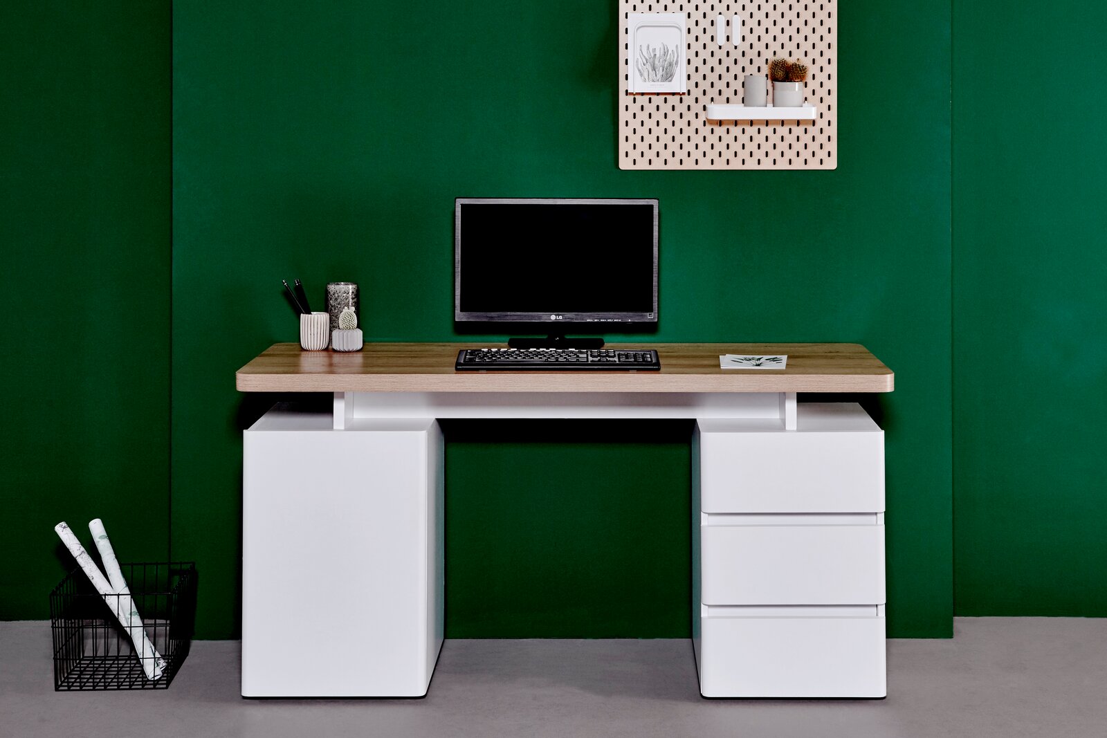 Moderner Schreibtisch mit Holzplatte und weißen Schubladen, frontal vor grünem Hintergrund fotografiert.