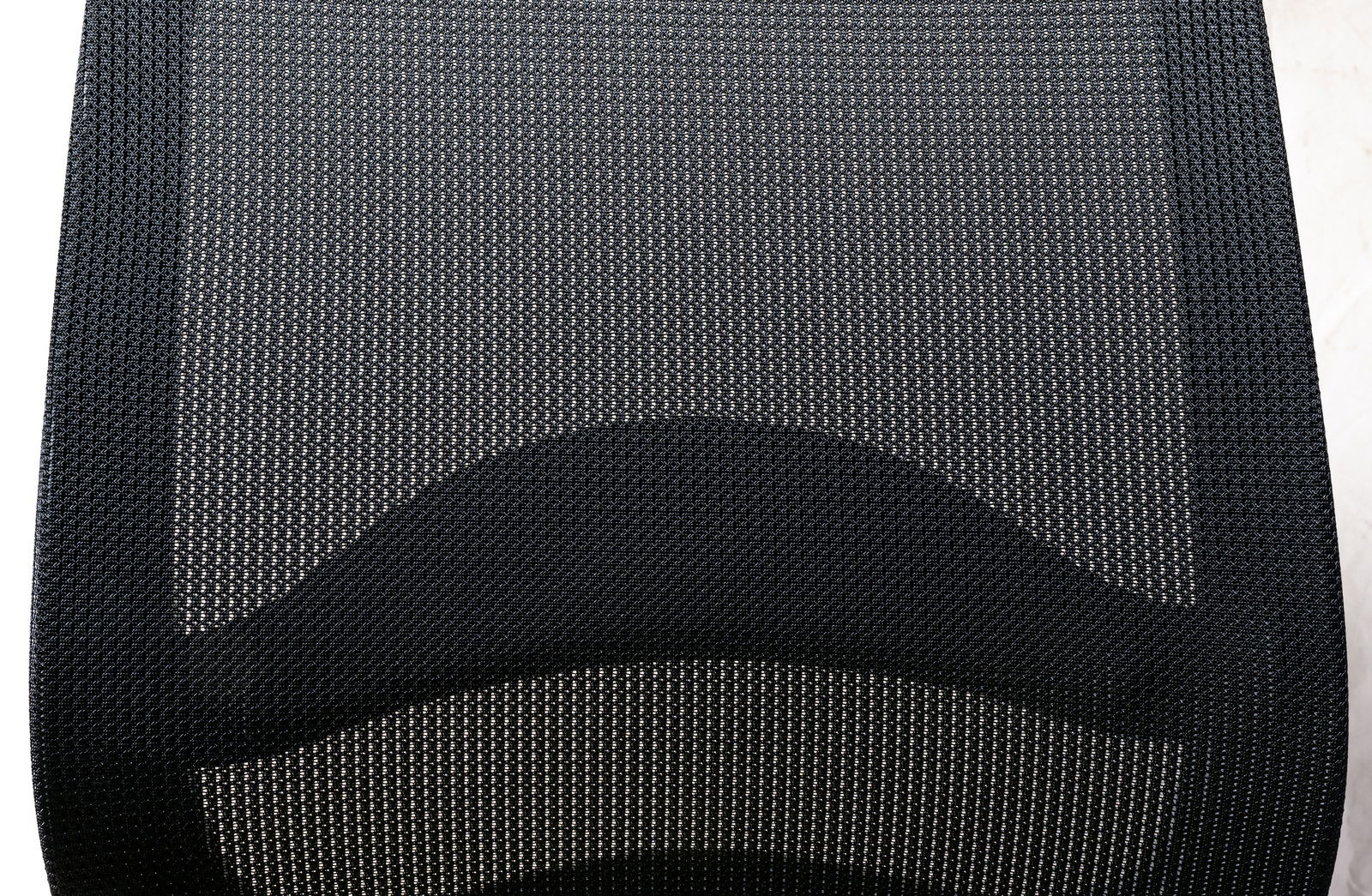 Nahaufnahme der Rückenlehne eines Drehstuhls aus schwarzem Netzgewebe, von oben betrachtet.