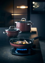 Pfanne FUSIONTEC Mineral 24 cm auf einem Herd mit brennender Flamme, gefüllt mit gebratenem Gemüse, in einer modernen Kücheneinstellung, seitliche Perspektive