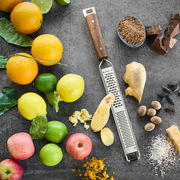 Fein- und Grobreibe mit Holzgriff, umgeben von frischen Früchten und Gewürzen, aus der Vogelperspektive.