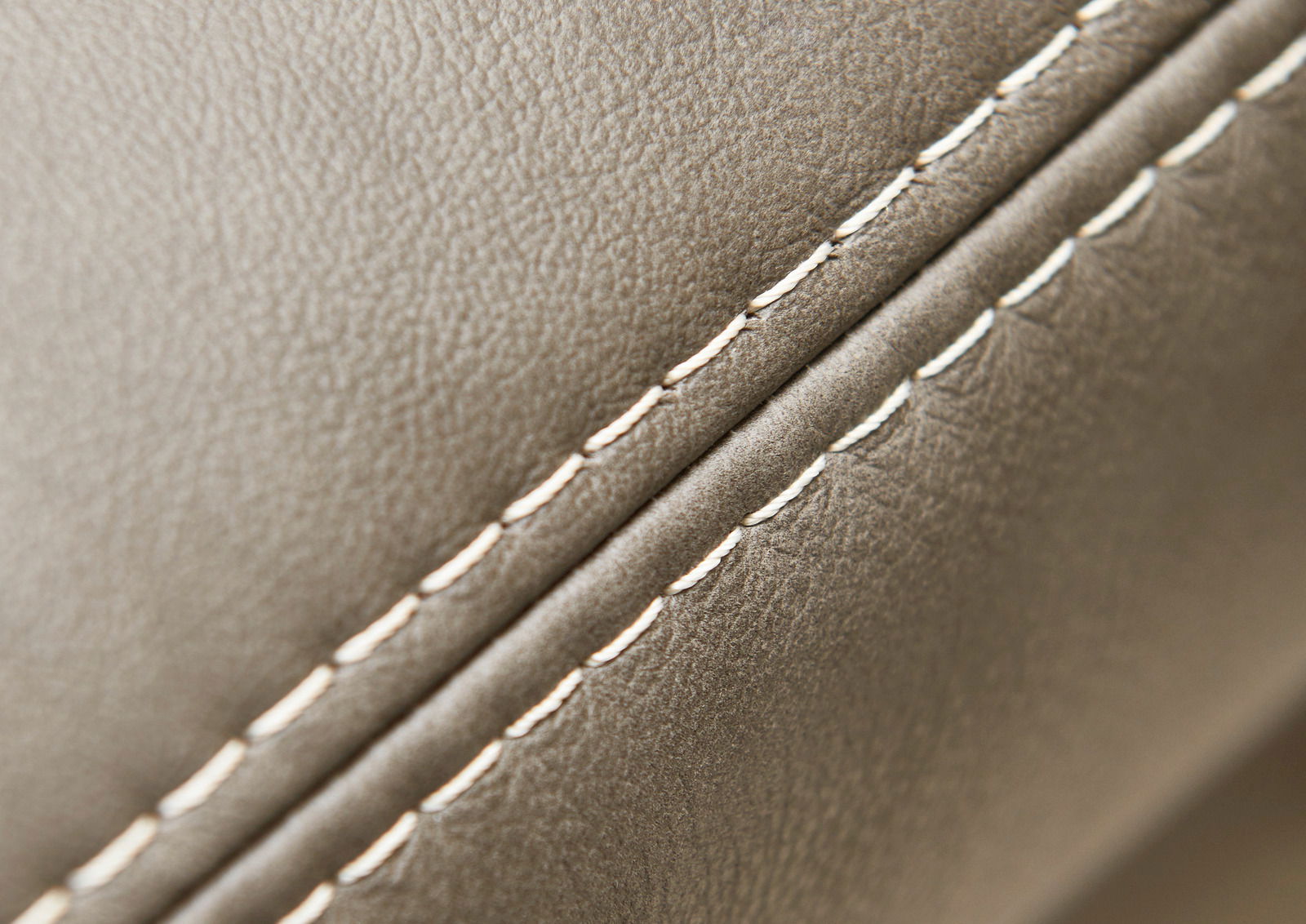 Nahaufnahme einer Polsterrundecke mit feiner Naht und glatter, beiger Lederoberfläche, seitliche Perspektive.