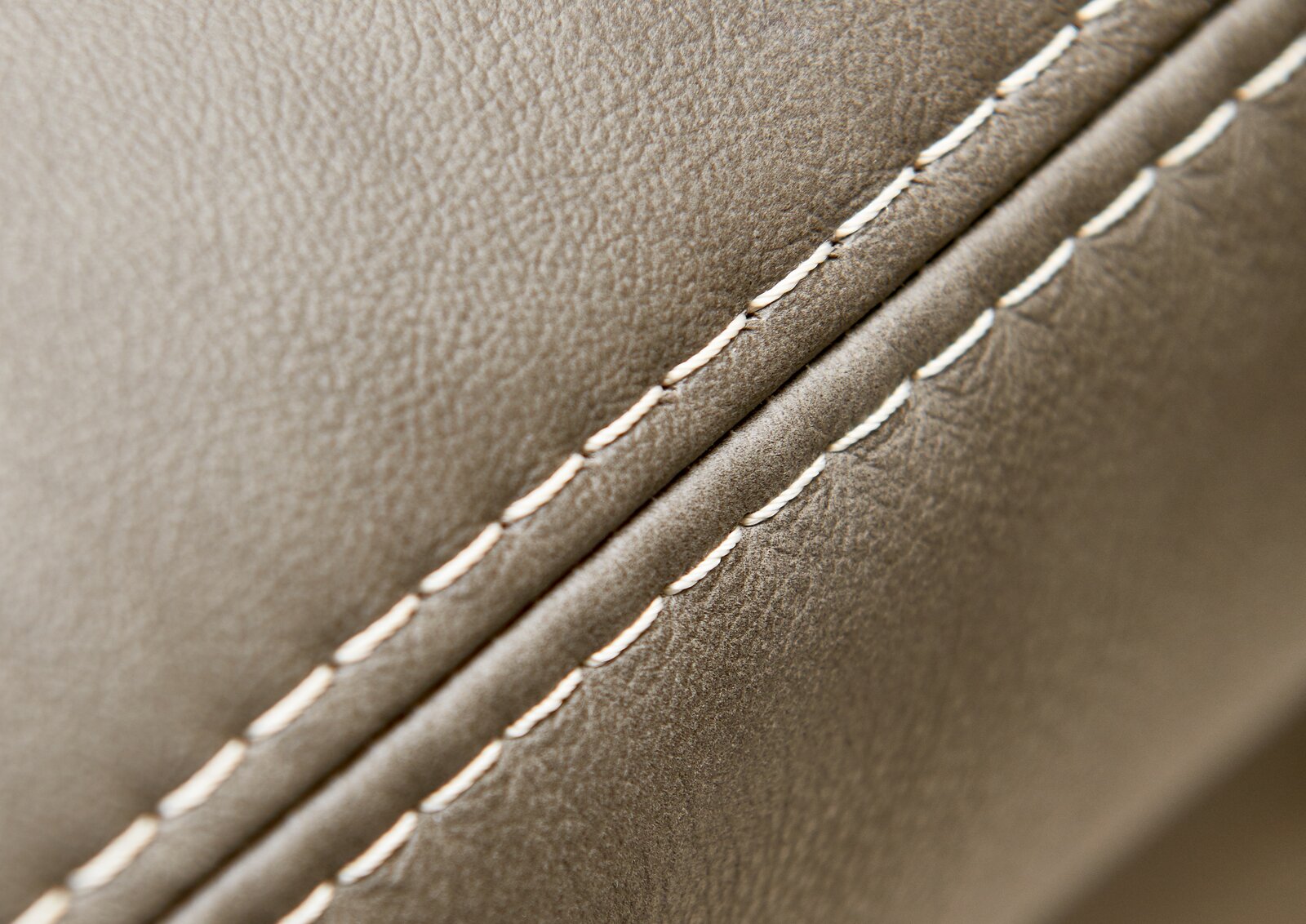 Nahaufnahme einer Polsterrundecke mit feiner Naht und glatter, beiger Lederoberfläche, seitliche Perspektive.