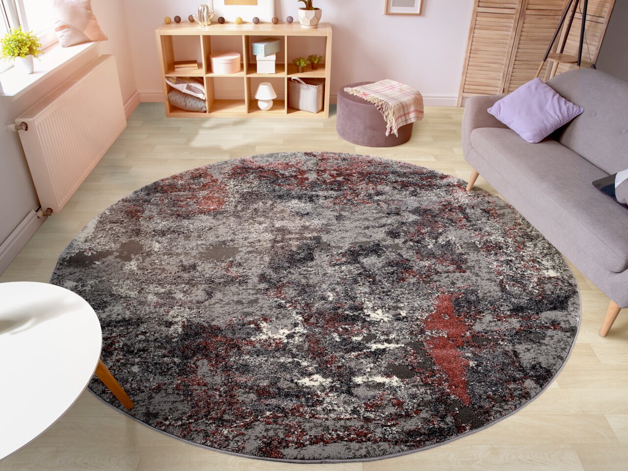 Runder Designer Teppich in einem modernen Wohnzimmer, mit abstraktem Muster in Grau- und Rottönen, aus der Vogelperspektive betrachtet.