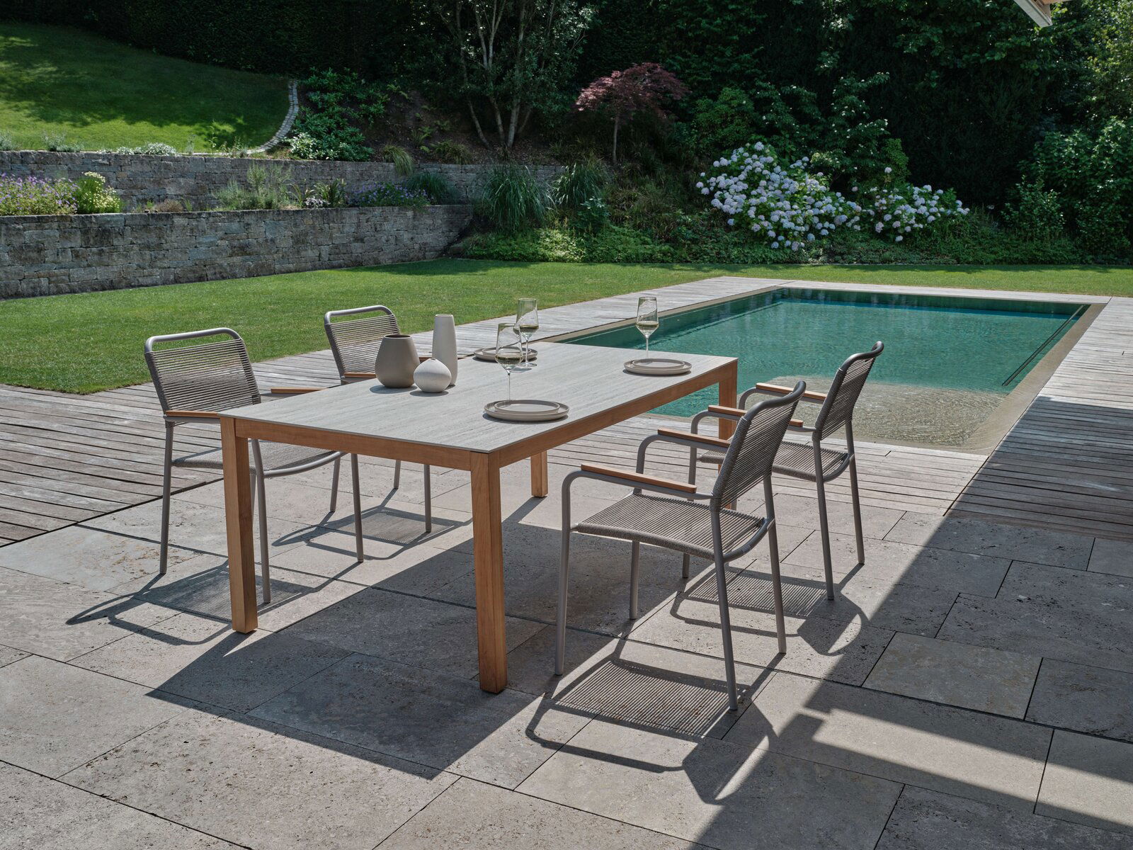 Moderner Stapelsessel auf einer Terrasse neben einem Pool, umgeben von einem gepflegten Garten. Perspektive von schräg oben.