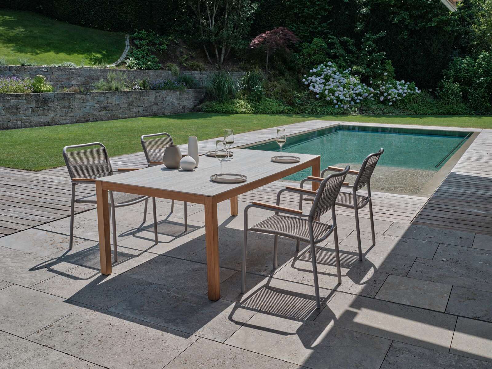 Moderner Stapelsessel auf einer Terrasse neben einem Pool, umgeben von einem gepflegten Garten. Perspektive von schräg oben.