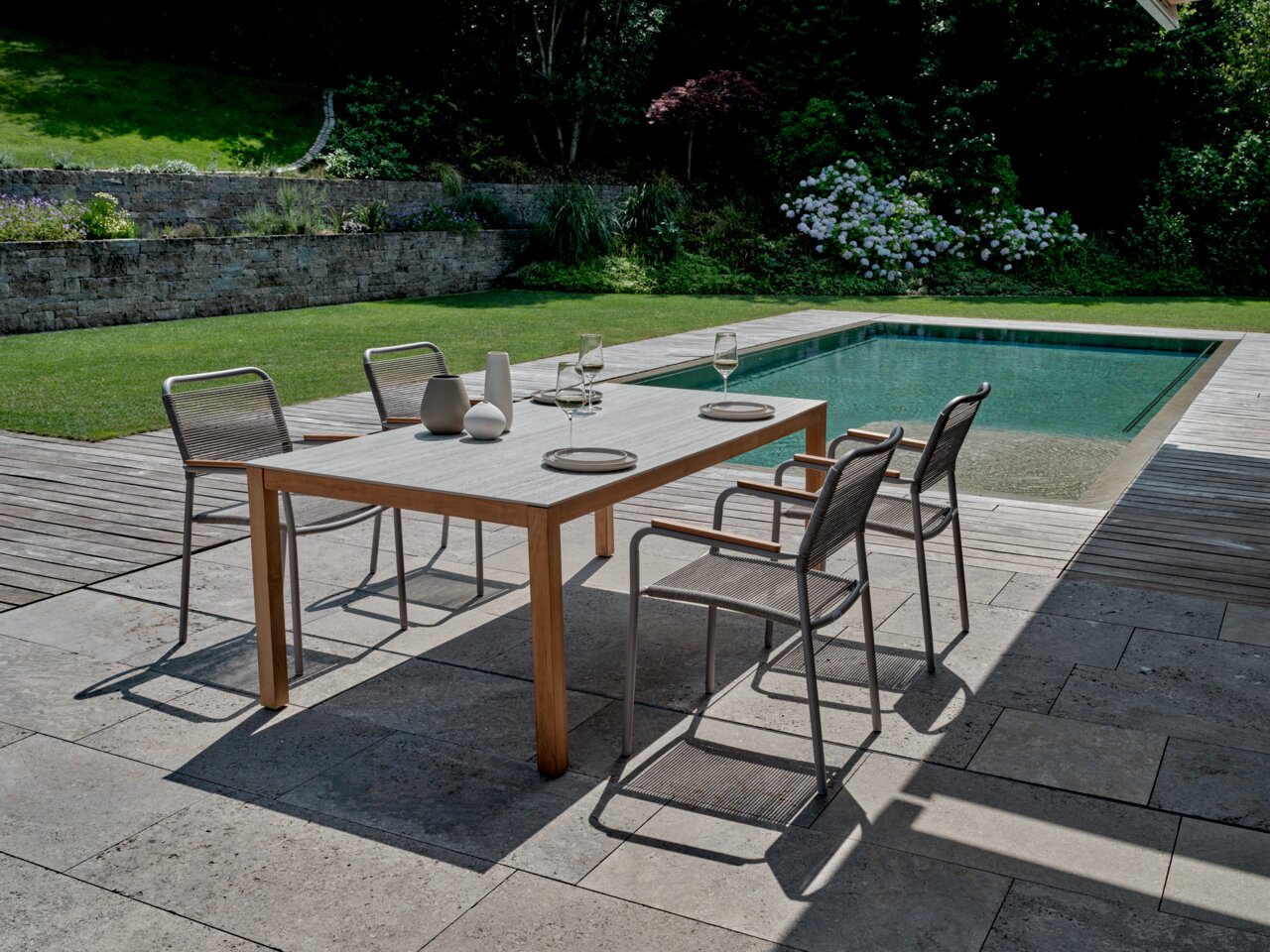 Moderner Stapelsessel auf einer Terrasse neben einem Pool, umgeben von einem gepflegten Garten. Perspektive von schräg oben.