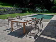 Moderner Stapelsessel auf einer Terrasse neben einem Pool, umgeben von einem gepflegten Garten. Perspektive von schräg oben.