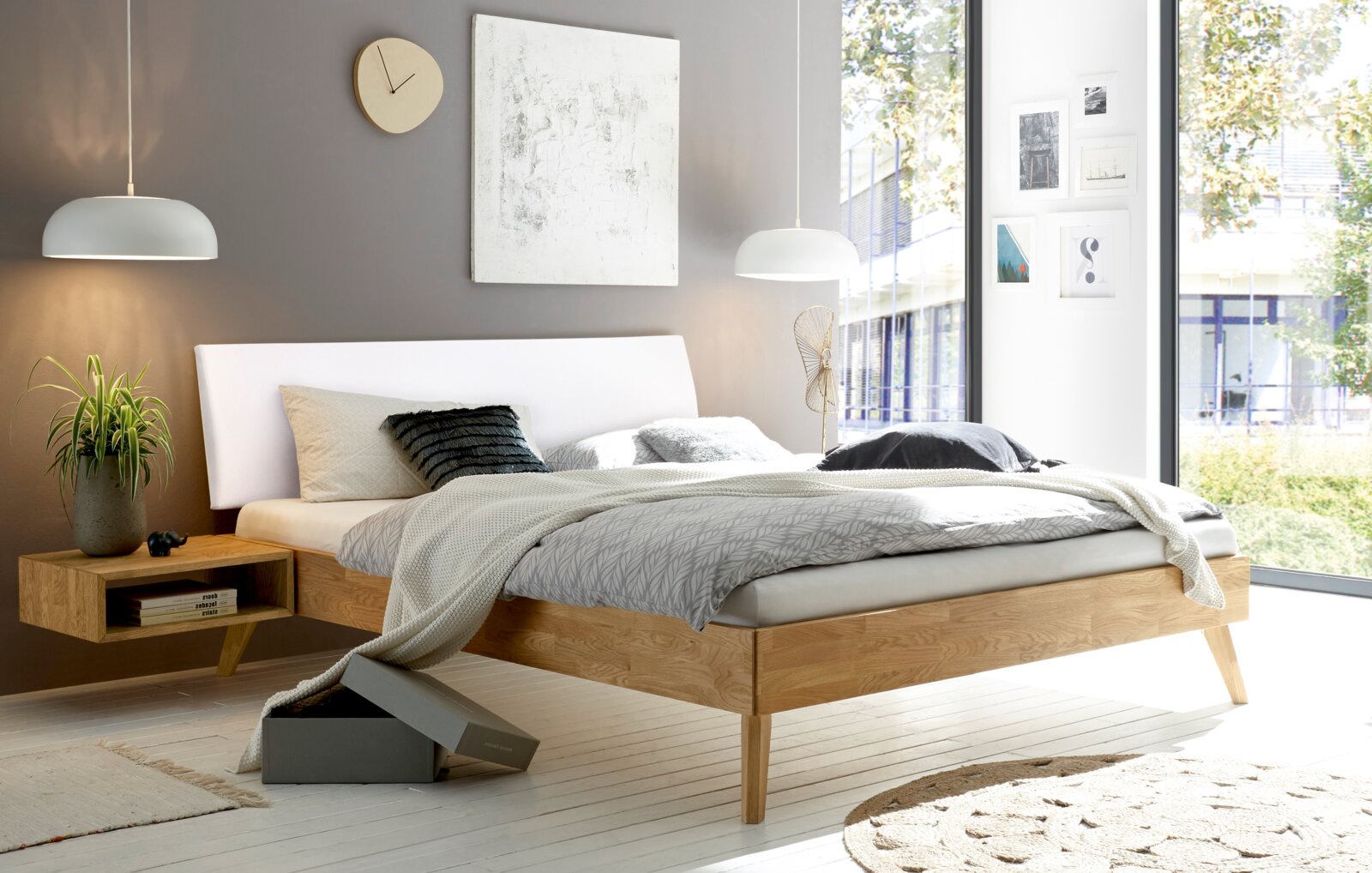 Modernes Schlafzimmer mit gepolstertem Kopfteil in einem hellen Raum mit großen Fenstern, seitliche Perspektive