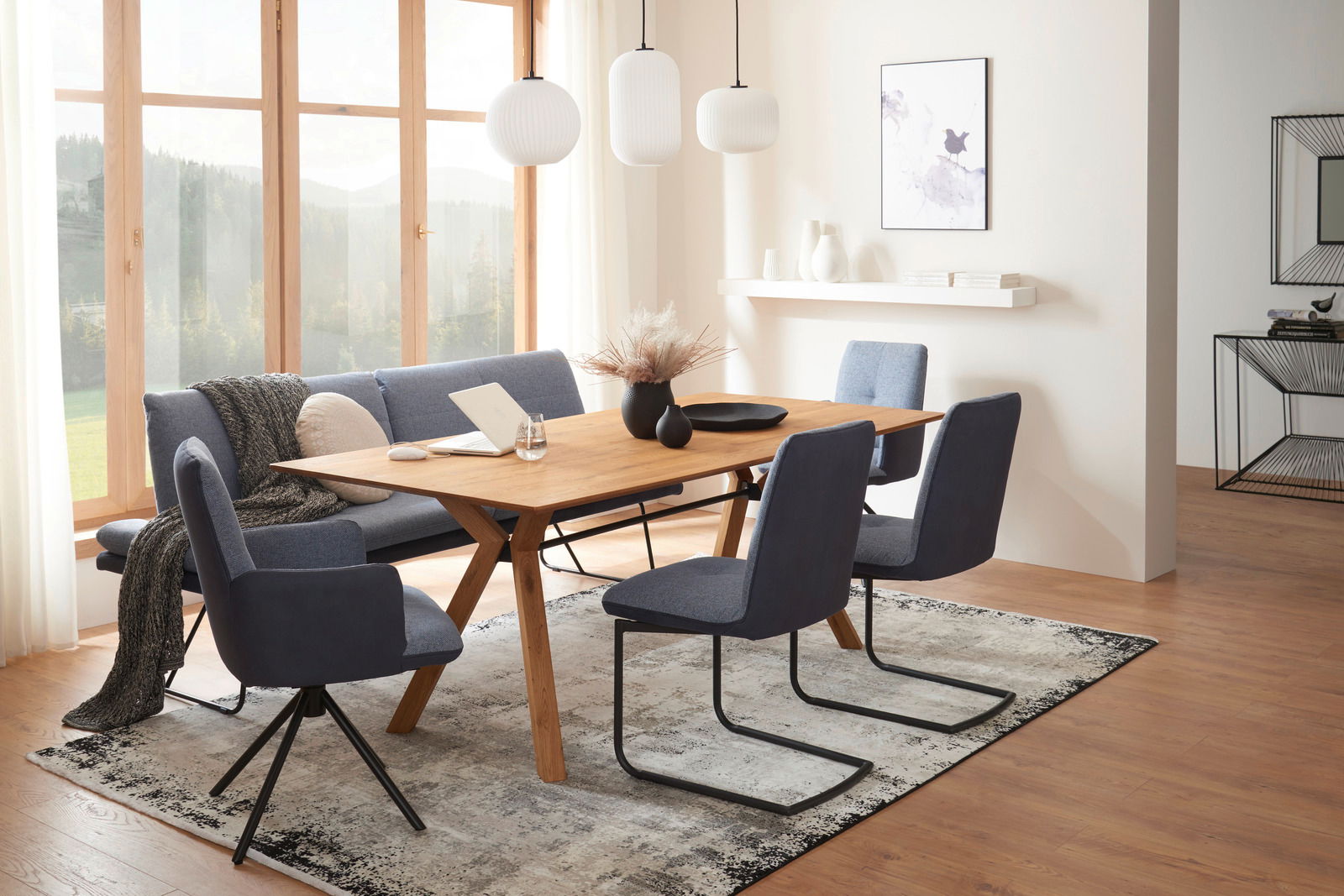 Moderner Esstisch aus Holz mit blauen Stühlen in einem hellen Esszimmer, seitliche Perspektive.