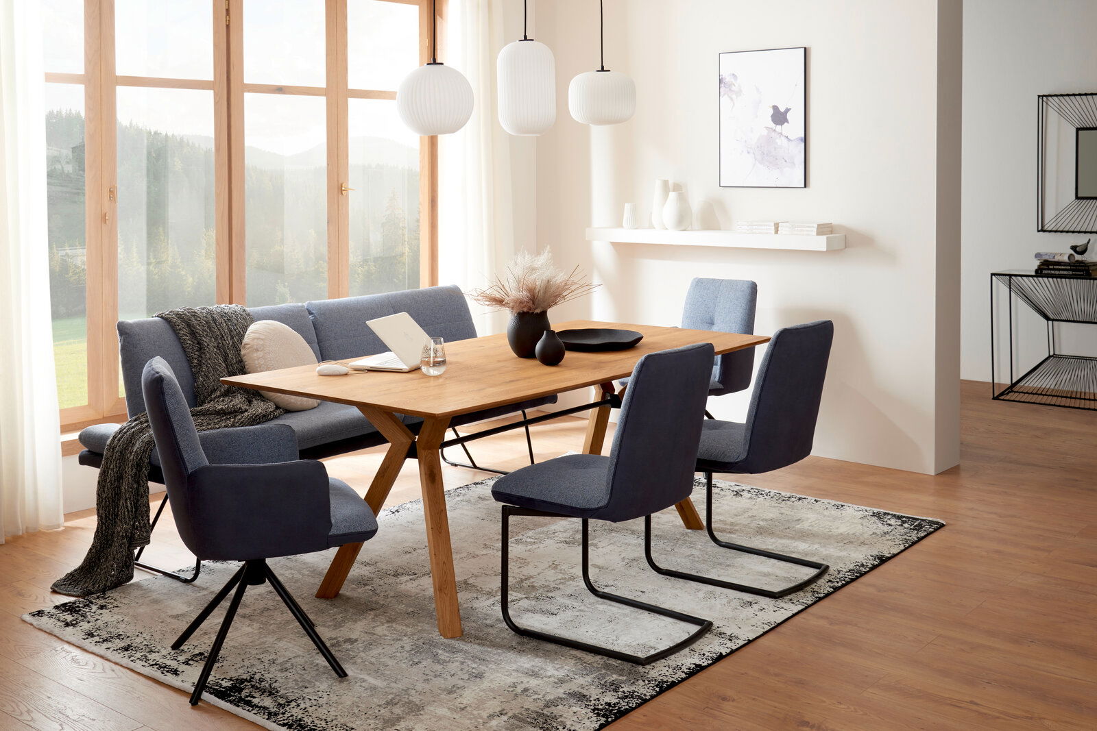 Moderner Esstisch aus Holz mit blauen Stühlen in einem hellen Esszimmer, seitliche Perspektive.