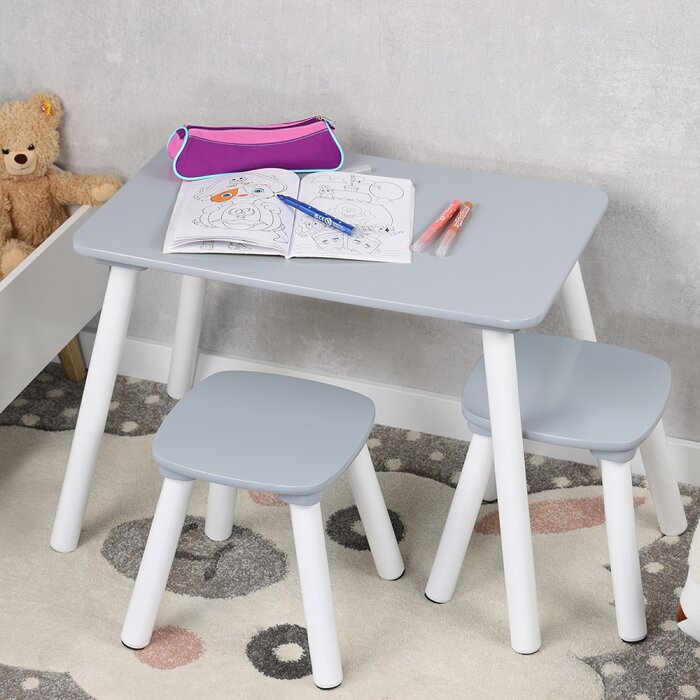 Grauer Kinder-Schreibtisch mit zwei passenden Hockern, weiße Beine, darauf Malbuch, Stifte und pinkes Mäppchen Perspektive: leicht von oben in schräger Vorderansicht