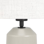 Close-up van een CAPALBIO-tafellamp met een gestructureerde, crèmekleurige voet en een lichte stoffen kap.