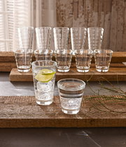 Becherset Wave 12-tlg. aus Glas, bestehend aus verschiedenen Größen, auf rustikalen Holzplatten präsentiert, mit Eiswürfeln und Limettenscheibe in einem Glas, seitliche Perspektive.