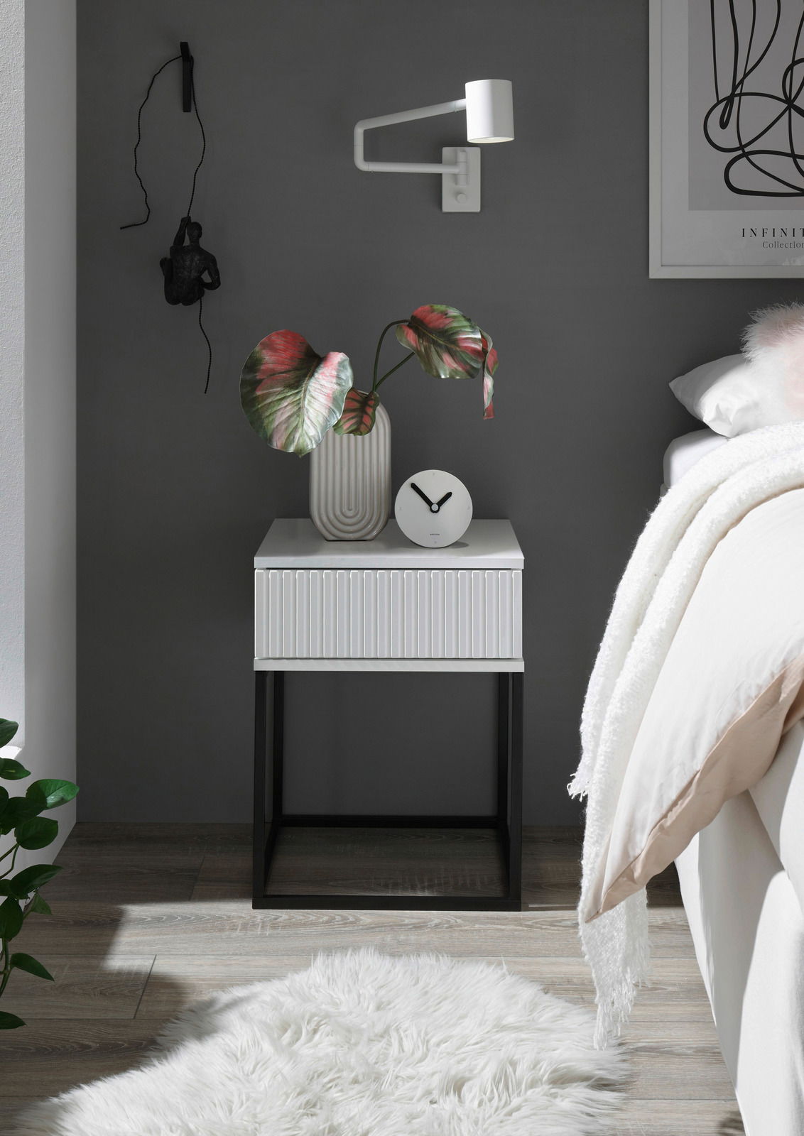 Z2 Nachtkommode MARLE Moderne Nachtkommode mit weißer Oberfläche und schwarzen Metallbeinen, dekoriert mit einer Vase und einer Uhr, seitliche Perspektive.