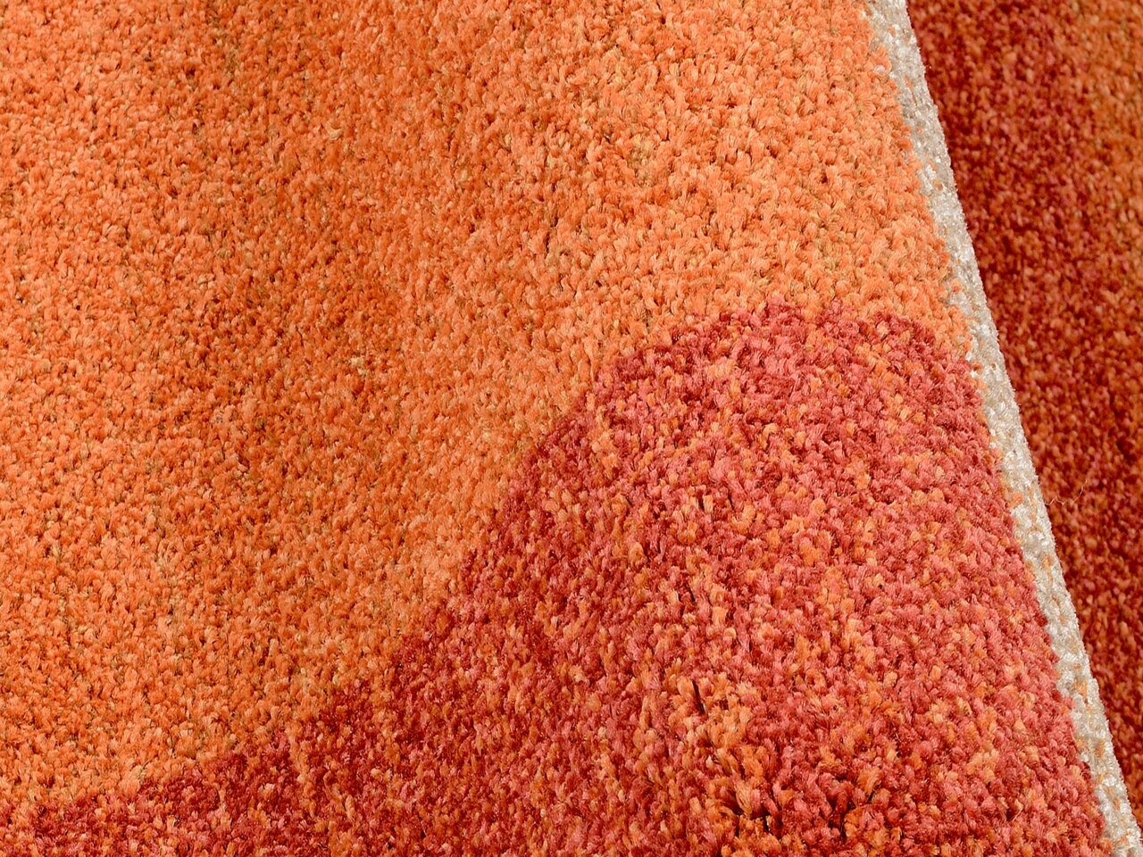 Nahaufnahme eines orange-roten Teppichs mit weicher Textur, perspektivisch von der Seite aufgenommen.