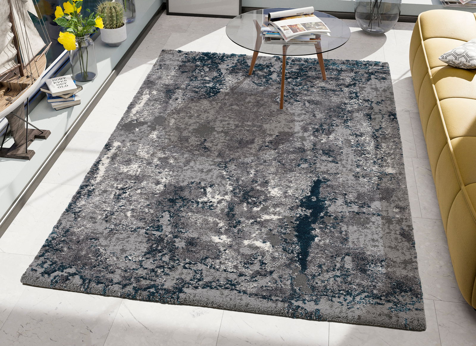 Moderner Designer Teppich in Grau- und Blautönen, fotografiert aus der Vogelperspektive, neben einem gelben Sofa und einem Glastisch.